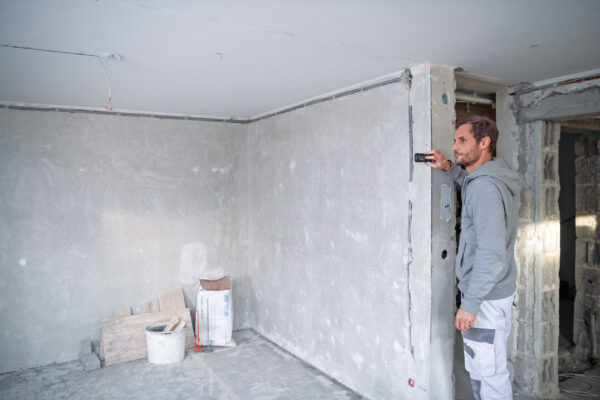 Worker using a Bosch 50m laser measure to calculate room dimensions on a construction site.