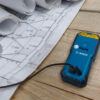 Close-up of the USB charging port on a Bosch 50m laser measure next to site plans.
