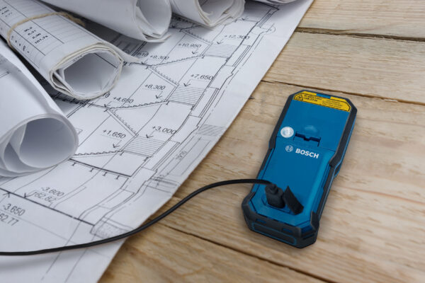 Close-up of the USB charging port on a Bosch 50m laser measure next to site plans.